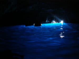 Hidden sea cave illuminated by blue light with natural rock formations and entrance to the open ocean, perfect for exploring underground coastal landscapes.