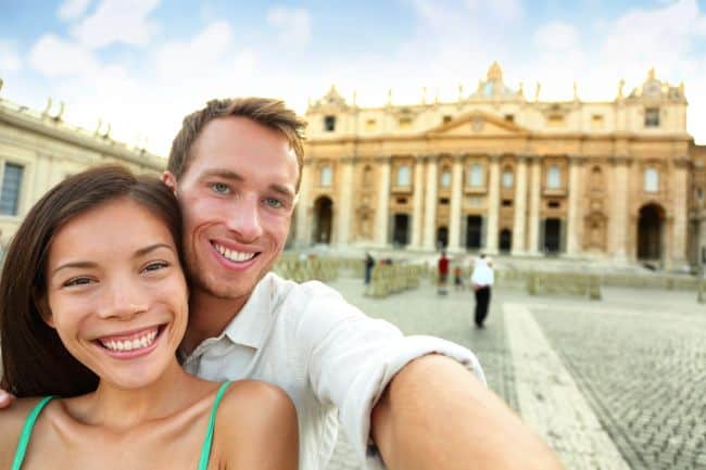 Vibrant couple taking selfie in front of historic Italian architecture, showcasing Italy travel, culture, and sightseeing experiences at a famous landmark.