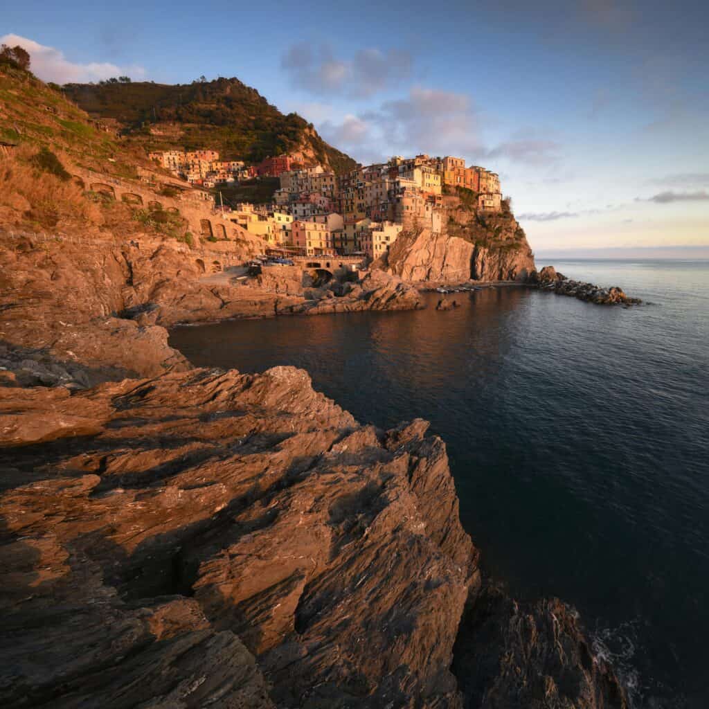 Scenic view of a colorful coastal village perched on cliffs overlooking the sea at sunset, showcasing Italy's picturesque seaside charm.
