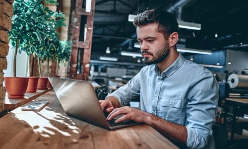 A professional man working on a laptop in a modern office environment, representing Win³ Partnerships. The image highlights teamwork, innovation, and strategic business alliances.