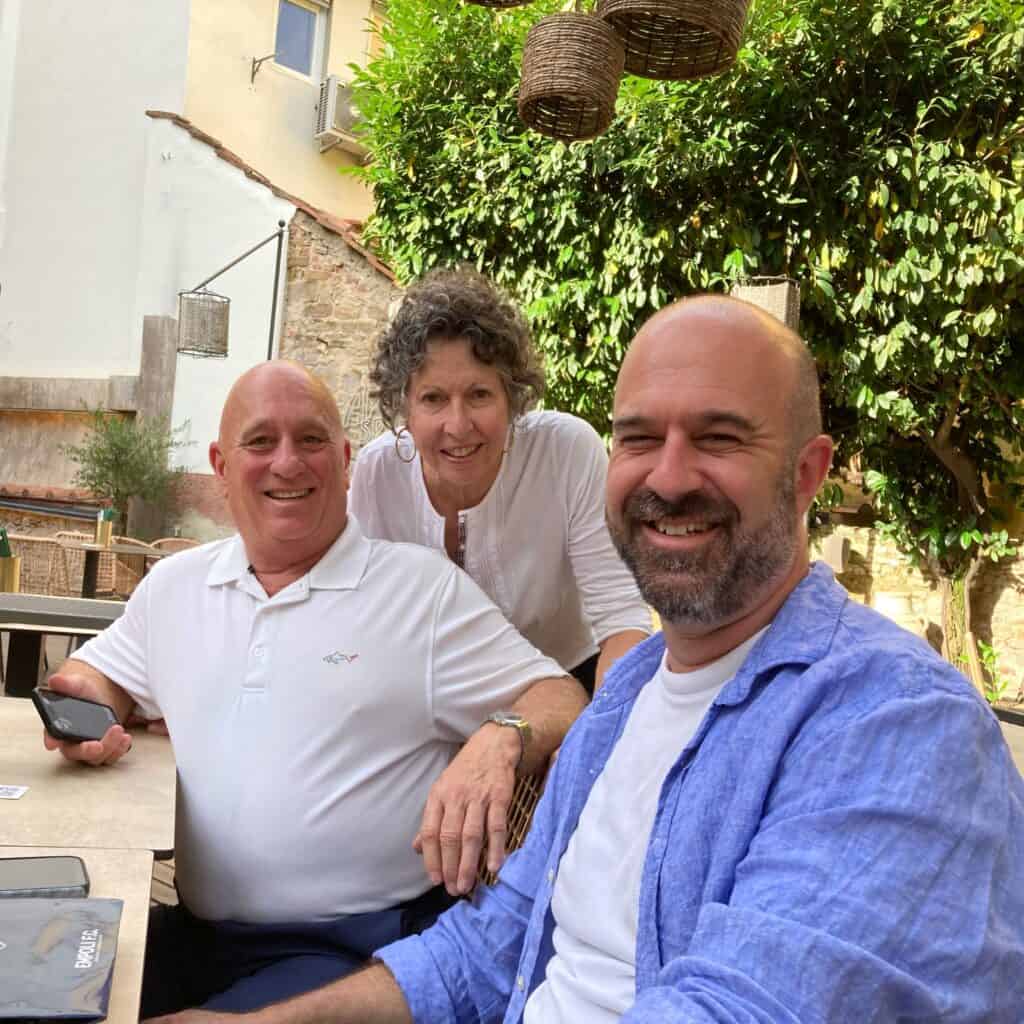 Smiling group of three enjoying a sunny day outdoors in Italy, surrounded by lush greenery and rustic decor, capturing the essence of Italian leisure and friendship.