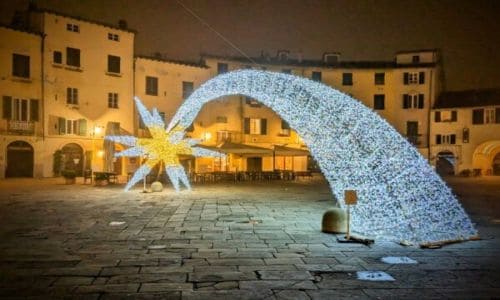 Bright illuminated star and comet-shaped light installation in a historic town square at night.
