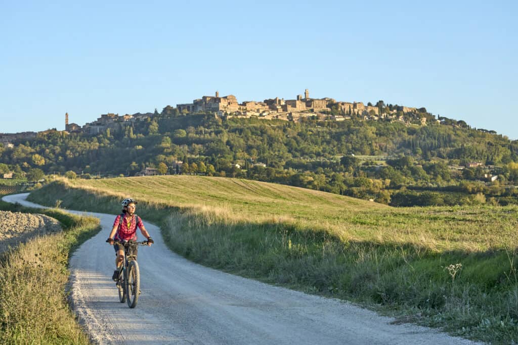 Cyclist riding on a scenic rural trail with a historic hilltop town in the background.