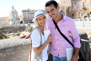 Happy couple sightseeing in Rome, Italy, with a laptop, enjoying the historic cityscape and sunny weather.