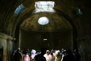 Group of tourists exploring an ancient underground tunnel with a circular opening in the ceiling, showcasing historical architecture.