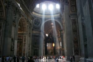 Sunlight streams through the dome of St. Peter's Basilica illuminating the grand interior with visitors exploring.